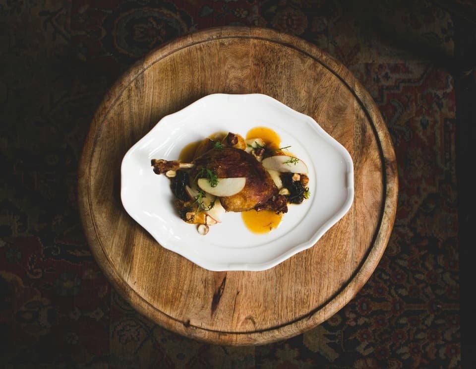 Cuisse de volaille rôtie, pommes et noisettes, dans une assiette blanche posée sur un plateau rond en bois, vue de dessus
