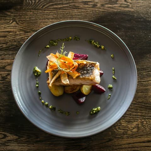 Poisson rôti, légumes d’automne et herbes dans une assiette en grès, vus de dessus