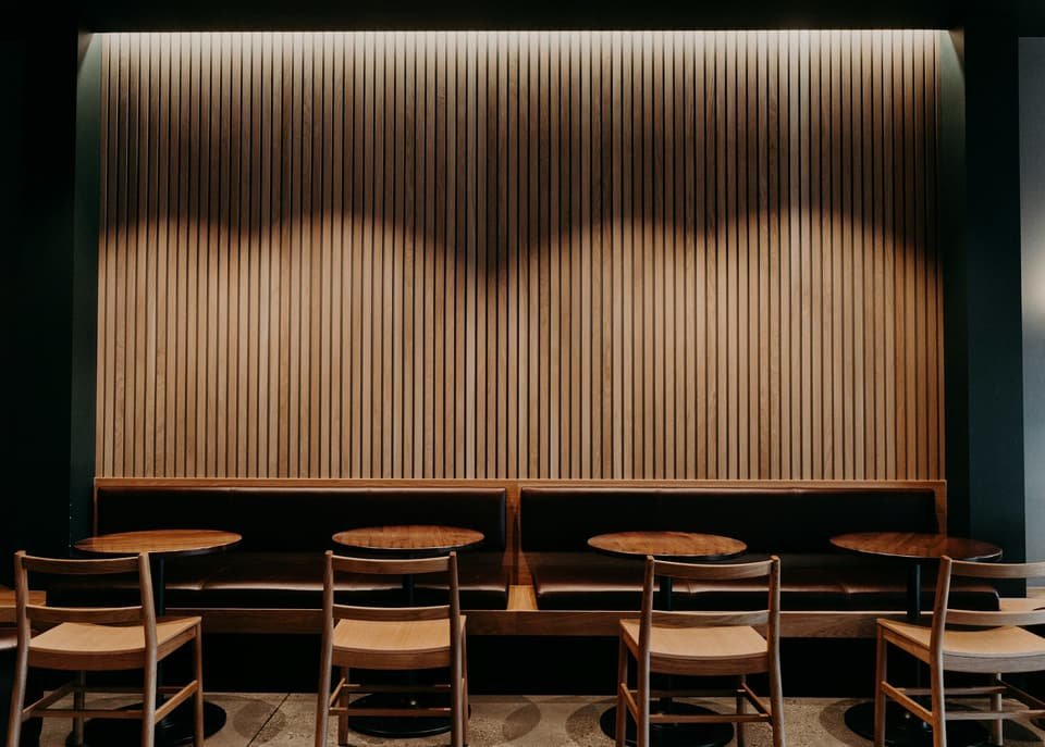 Banquette et tables en bois clair le long d’un mur à tasseaux de chêne